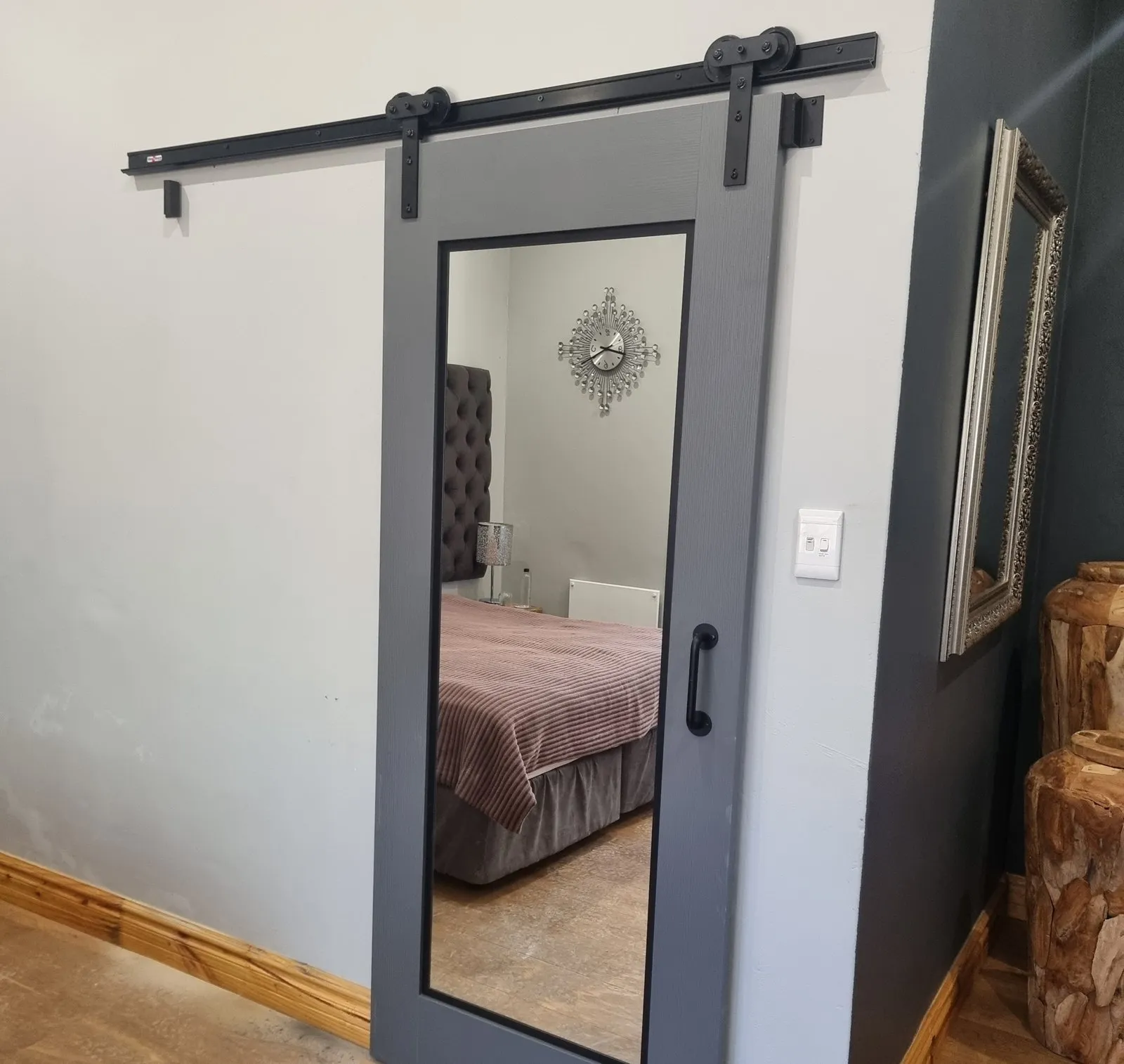 A grey mirrored door hung on a black sliding track in a guest room